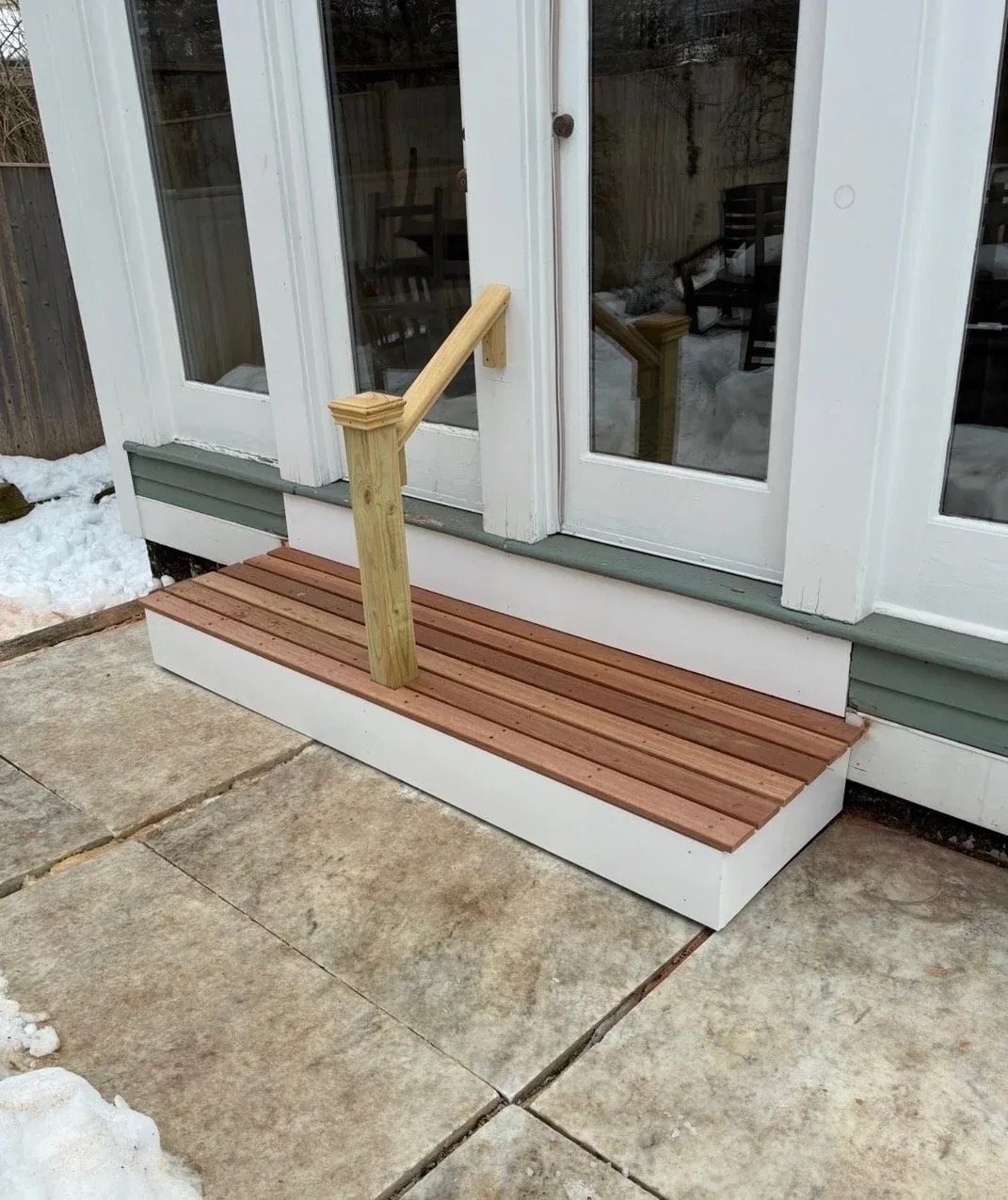 New cedar back step with a wooden handrail at a rear entry.